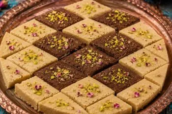 حلوا نخودچی دو رنگ با لایه‌های زعفرانی و کاکائویی تزئین شده با پودر پسته