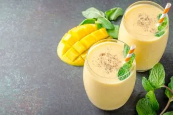 طرز تهیه میلک شیک انبه؛ لیوان میلک شیک انبه با رنگ زرد و بافت مخملی