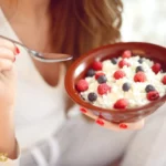 زن در حال خوردن پنیر کاتیج با توت‌ها
